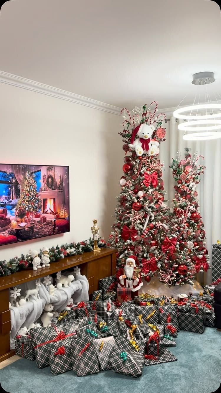 Two decorated Christmas trees with red bows surrounded by plaid wrapped gifts on the floor.