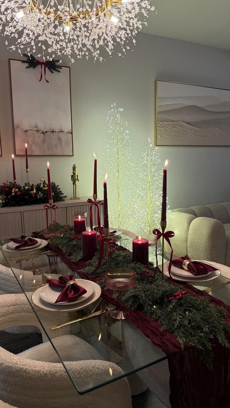 A festive dining table set with white plates, red napkins, and evergreen garland under a sparkling chandelier.