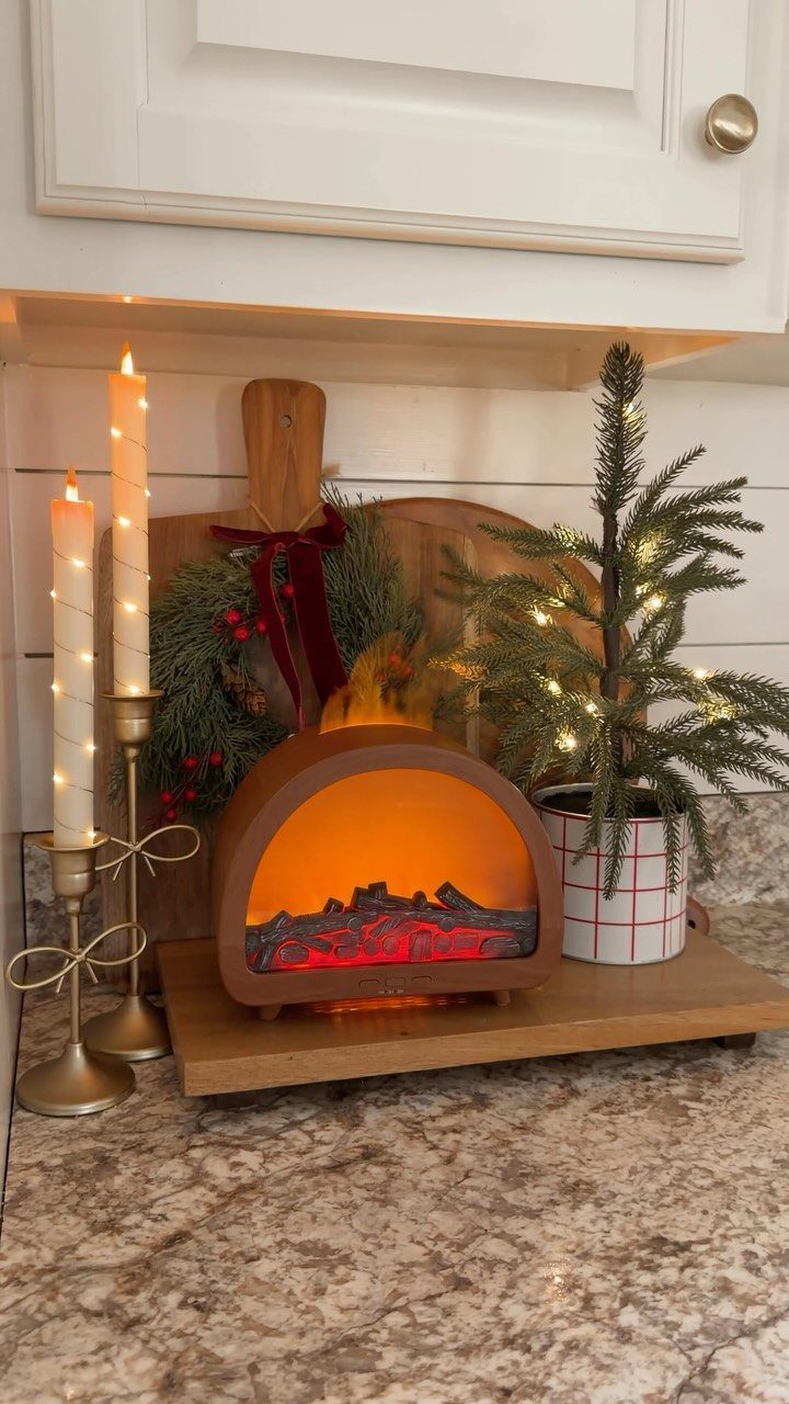 Festive holiday decor featuring a miniature electric fireplace, lit candles, and a small lighted evergreen tree.