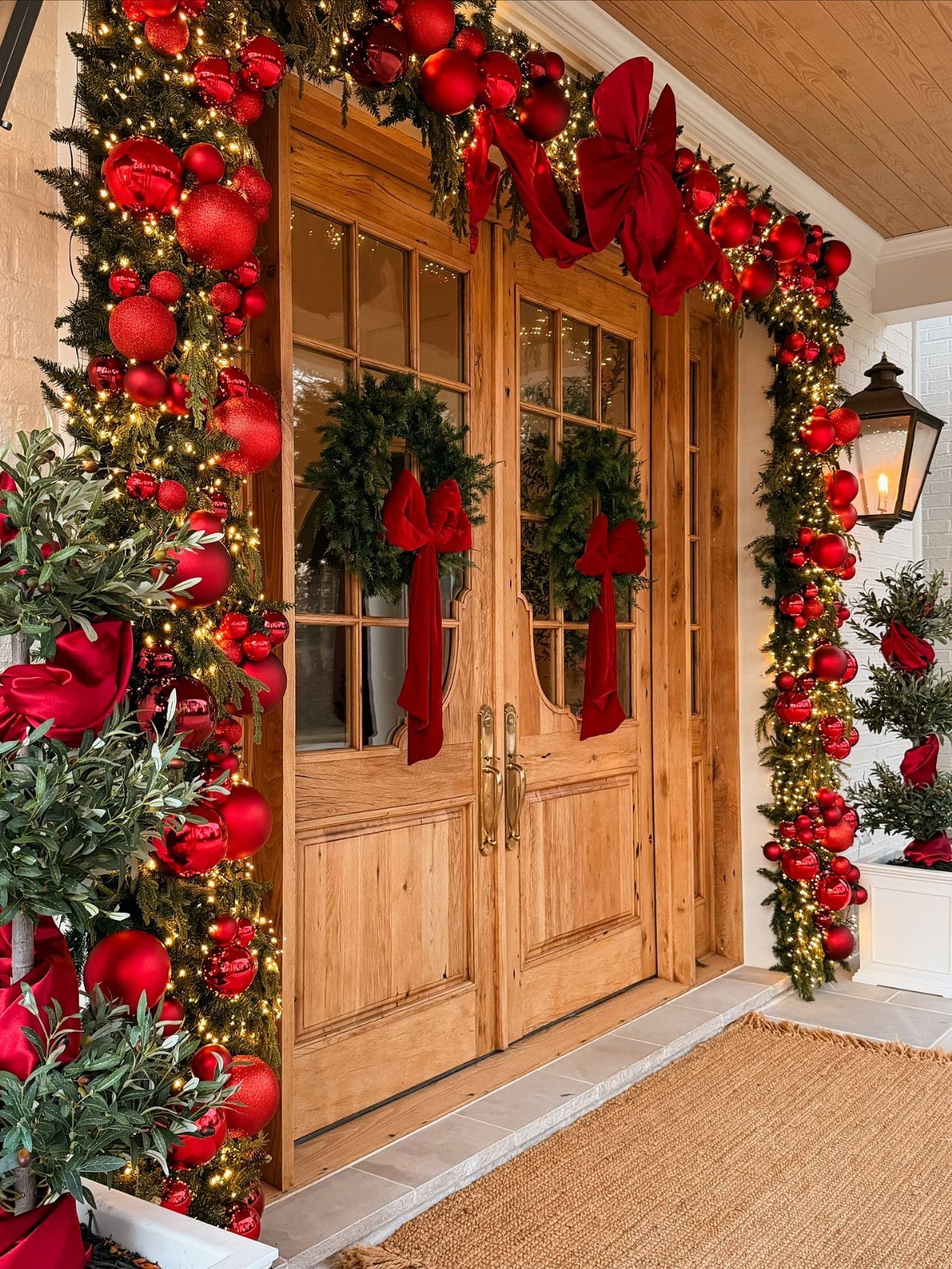 11 Classic Christmas Decor Ideas for Every Room in Your Home 1 Wooden double doors decorated with festive evergreen garlands, red ornaments, and large red bows.
