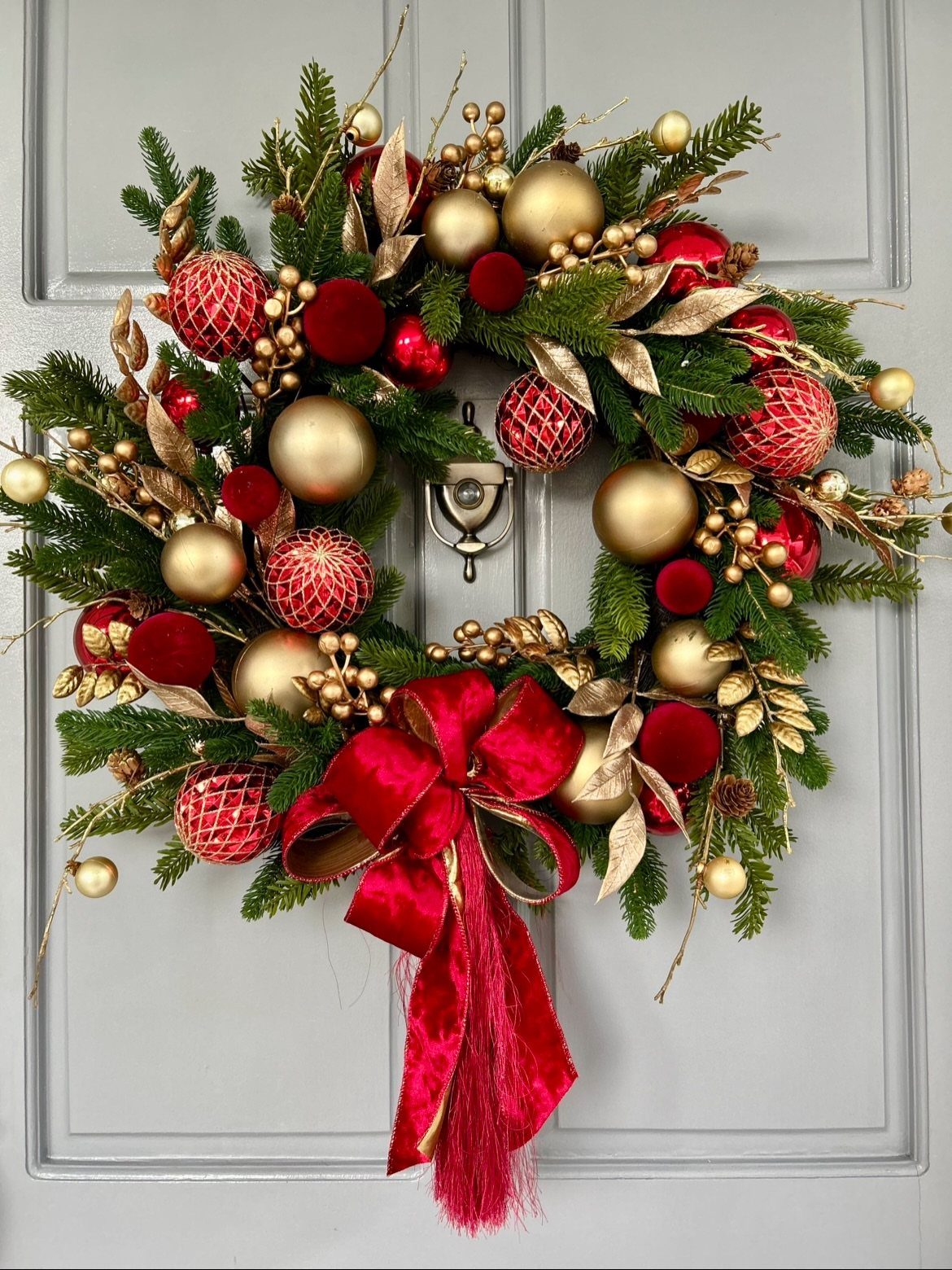 11 Classic Christmas Decor Ideas for Every Room in Your Home 6 A festive Christmas wreath with red and gold ornaments hanging on a grey door.