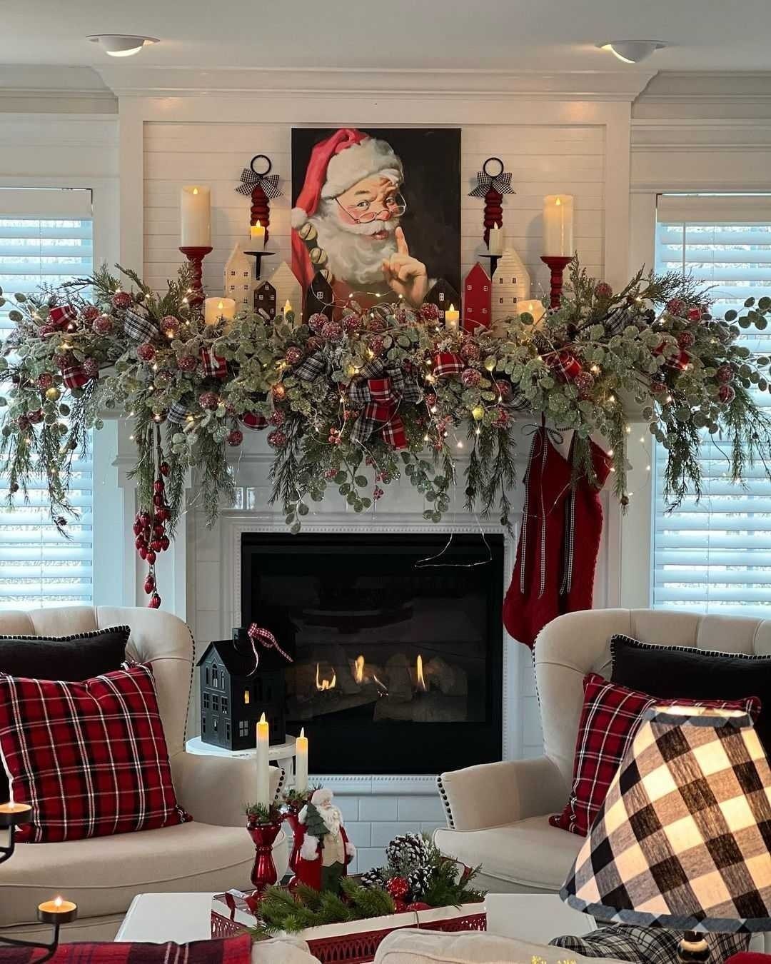 11 Classic Christmas Decor Ideas for Every Room in Your Home 2 A decorated white fireplace mantel featuring a Santa portrait, greenery, red stockings, and glowing candles.