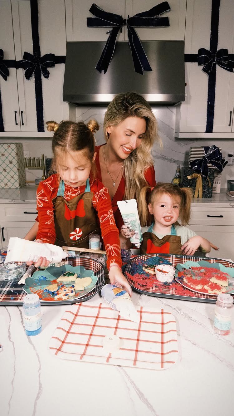 A woman and two children decorating Christmas cookies with colorful icing in a bright kitchen.