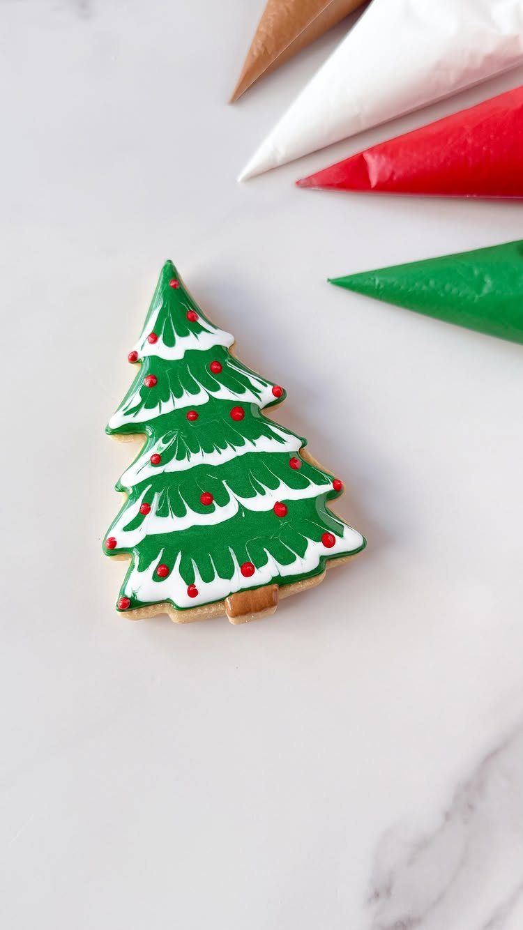A decorated Christmas tree cookie with green icing and red dots on a marble surface.
