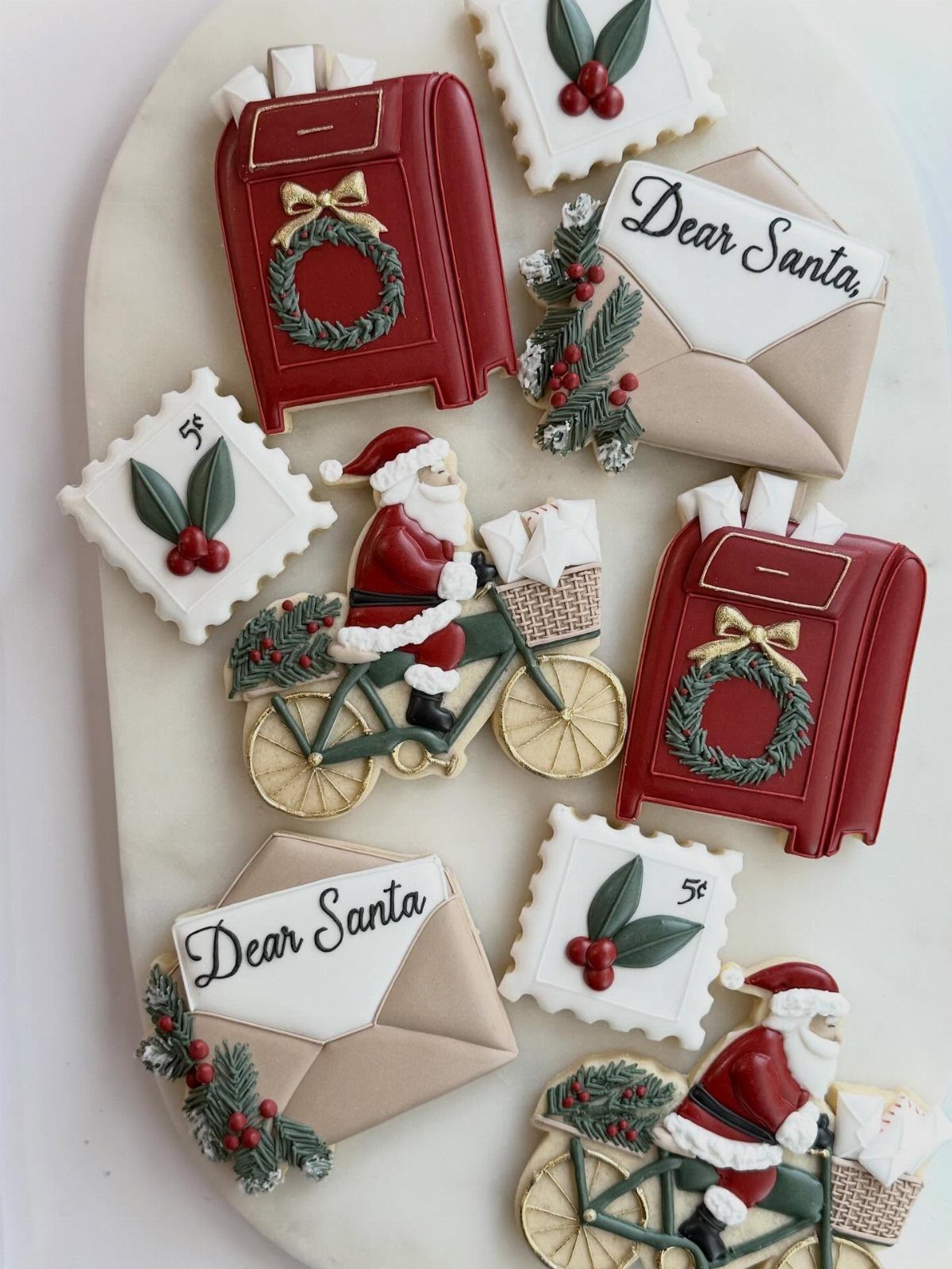 Decorated Christmas sugar cookies featuring Santa on a bicycle, red mailboxes, and envelopes on a white platter.