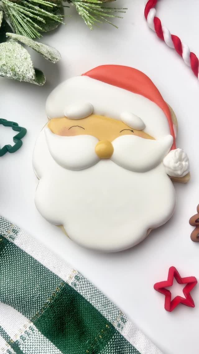 A decorated Santa Claus face sugar cookie on a white background with festive decorations.