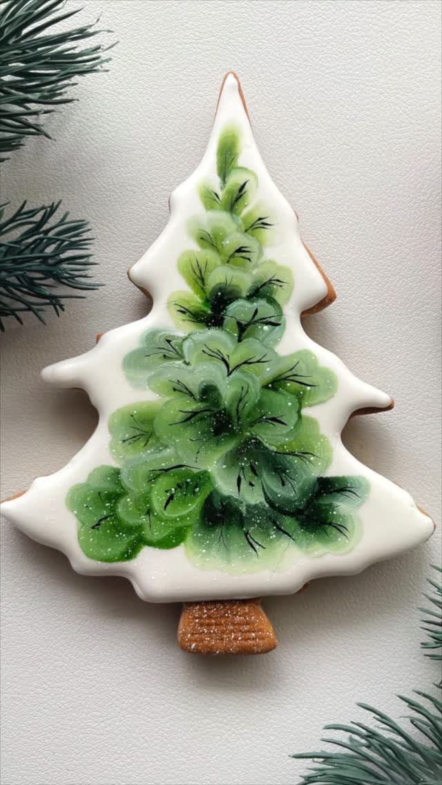 A Christmas tree shaped cookie decorated with green painted icing details on a white background.