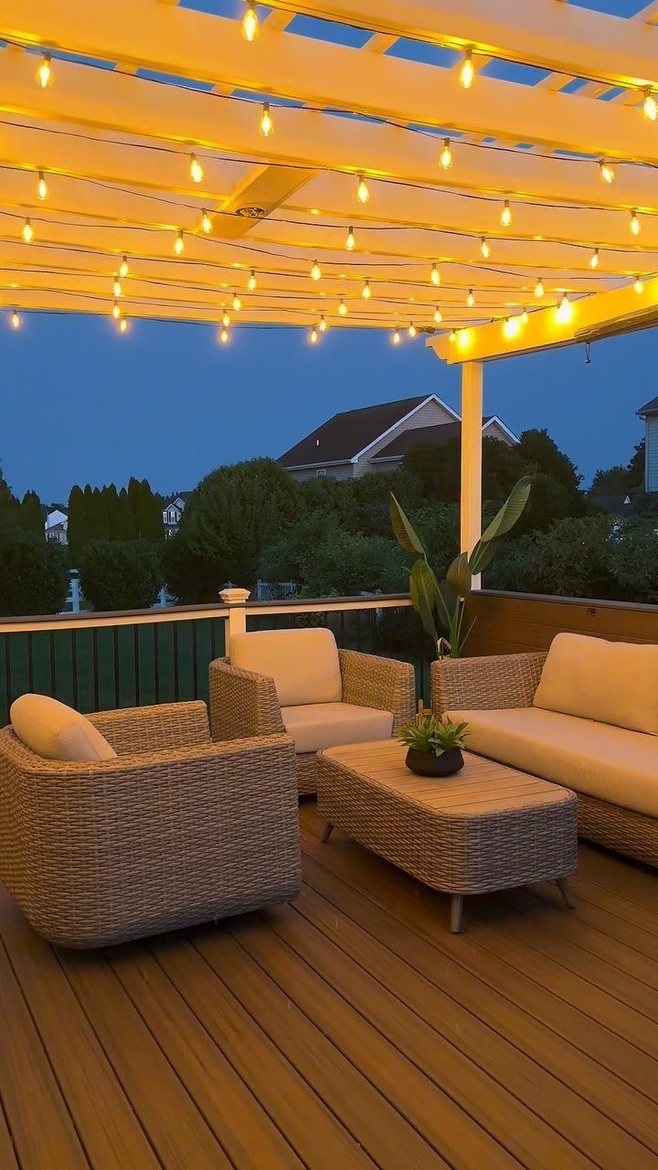 Wicker outdoor furniture set on a wooden deck under glowing string lights at dusk.