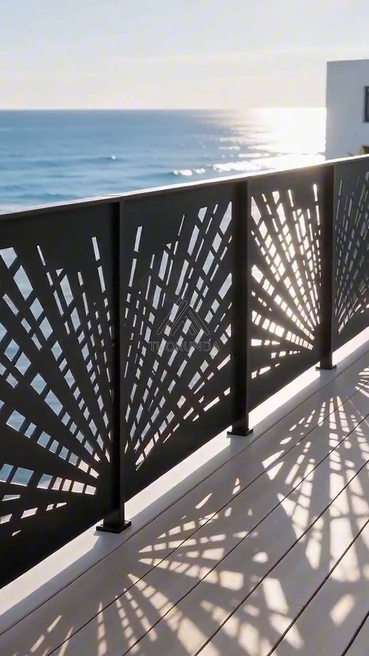 Black laser-cut sunburst pattern deck railings overlooking the ocean with sunlight casting shadows on the deck.