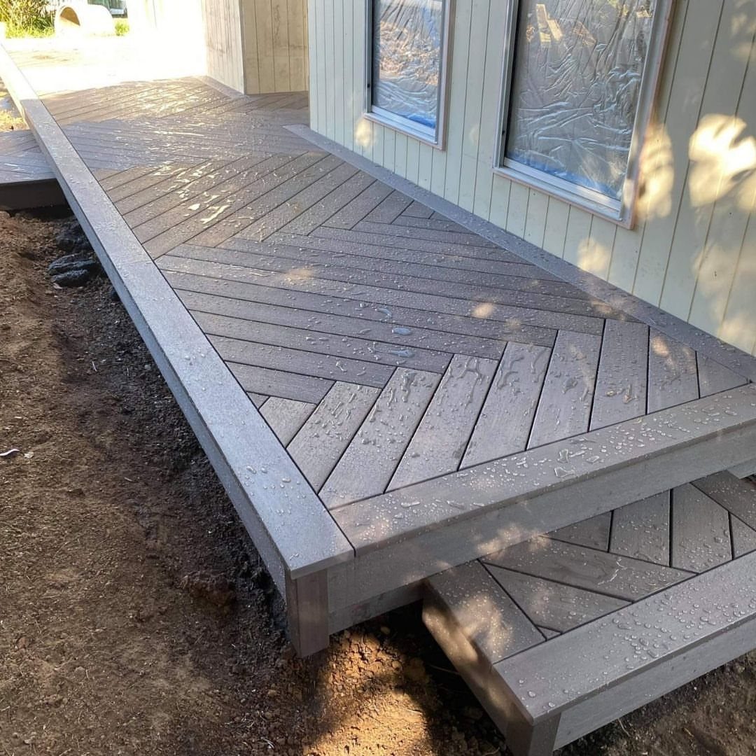 Grey wooden deck boards arranged in a decorative herringbone pattern next to a house wall.