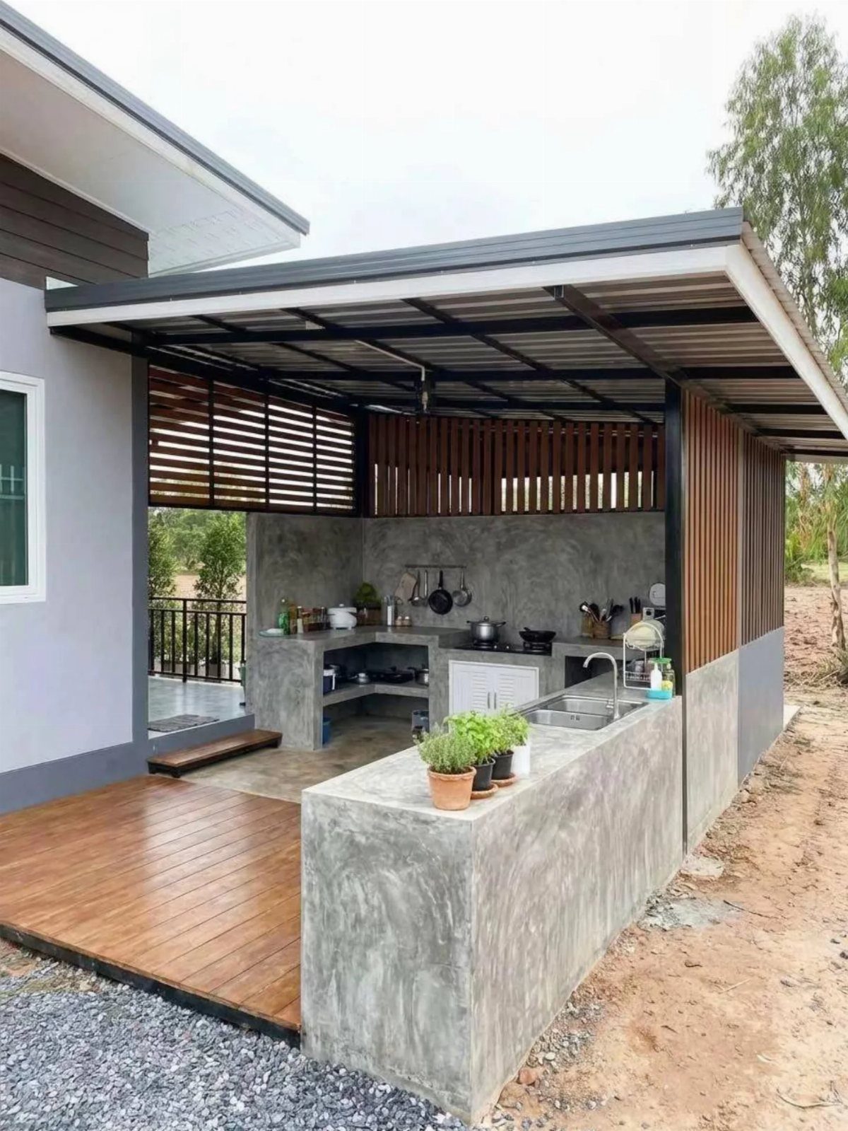 Concrete outdoor kitchen with built-in sink and stovetop under a modern metal roof structure.