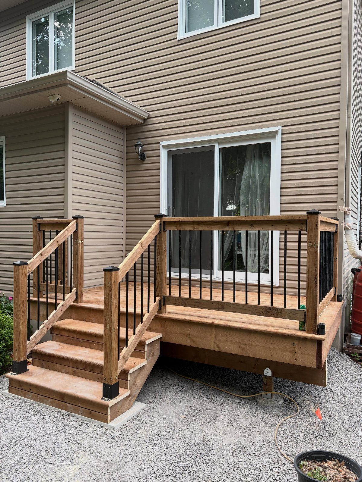 A wooden backyard deck with black metal railings and stairs attached to a tan sided house.