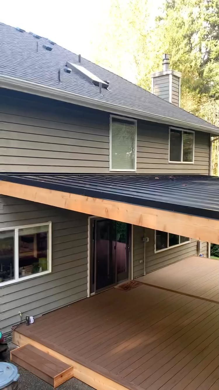 8 Deck with Roof Ideas for Every Backyard Layout 6 A dark metal roof structure covering a wooden deck attached to a grey house.