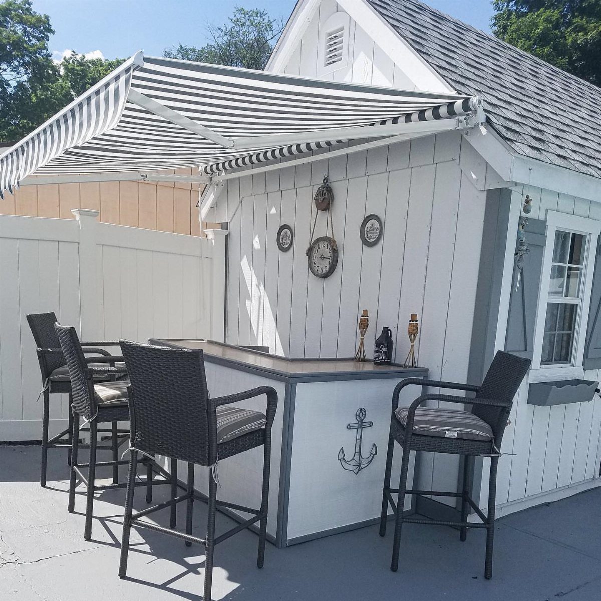 8 Deck with Roof Ideas for Every Backyard Layout 2 A striped retractable awning provides shade over an outdoor bar with wicker stools.