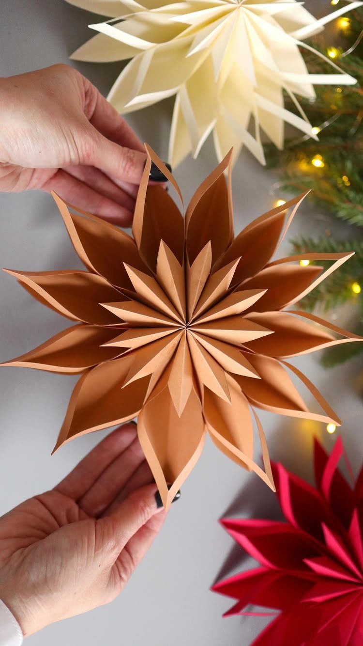 Hands holding a large, brown 3D origami star made from folded paper.