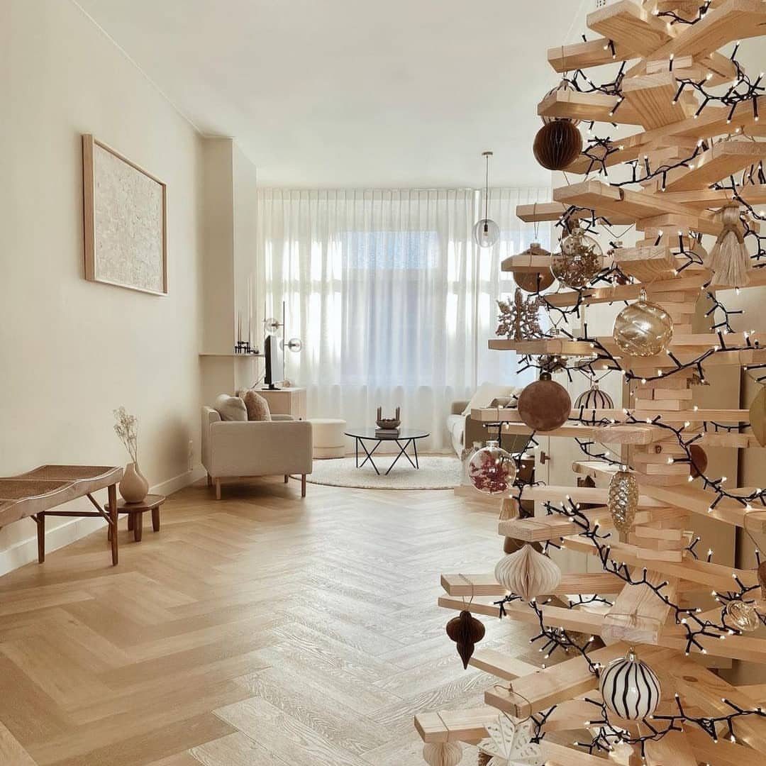 A minimalist Christmas tree made of stacked wooden slats decorated with ornaments and fairy lights.