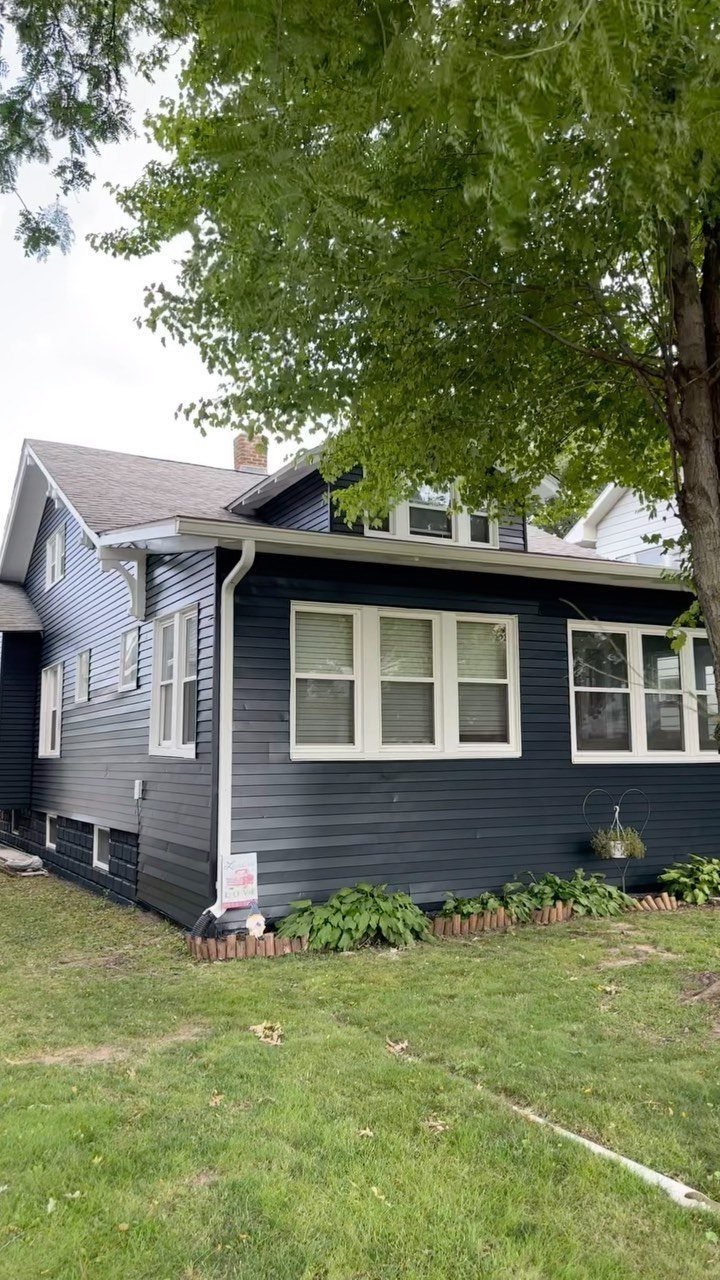 Exterior Color Ideas for 6 Home Styles 4 A dark blue house with white window trim sits behind a large green tree and lawn.
