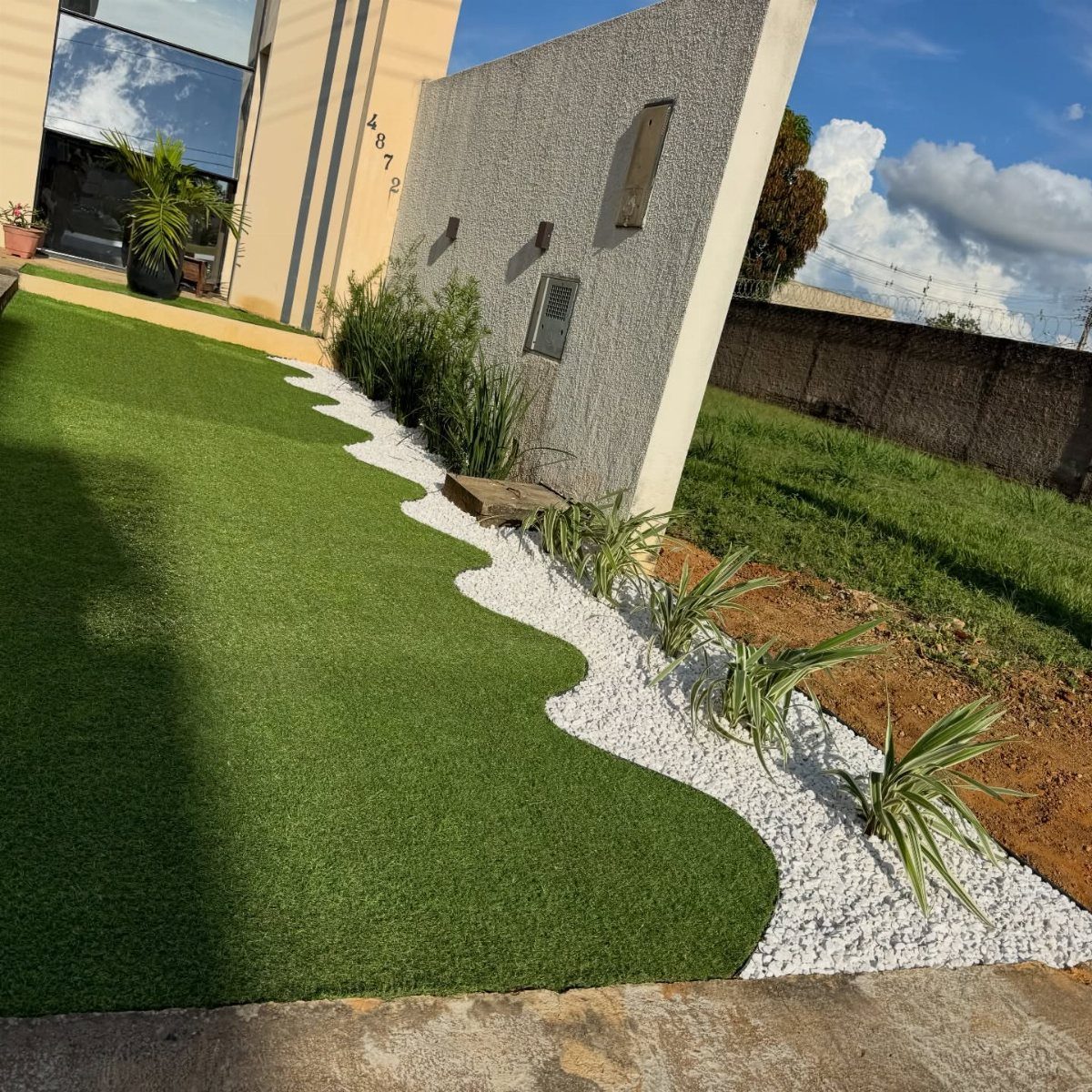 16 Front Lawn Landscaping Ideas for Curb Appeal 14 Artificial turf lawn with a wavy white gravel border and small green plants.