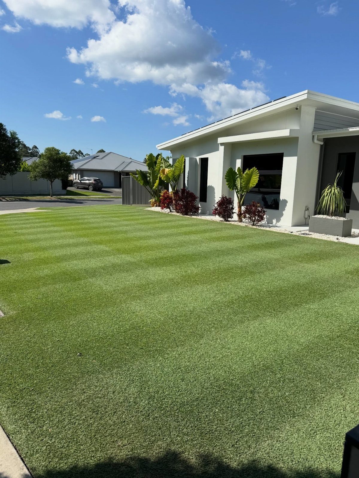 16 Front Lawn Landscaping Ideas for Curb Appeal 15 Striped green lawn in front of a modern white house with tropical garden beds.