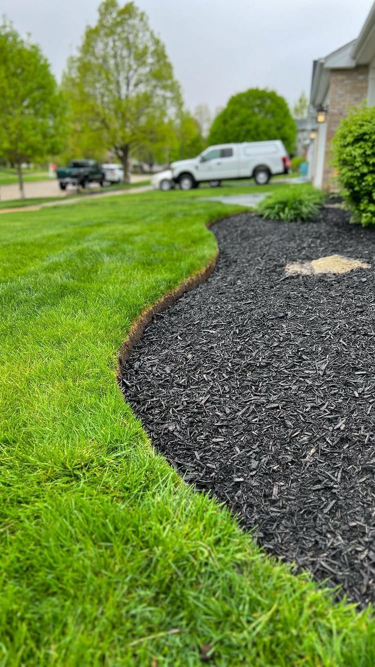16 Front Lawn Landscaping Ideas for Curb Appeal 1 Dark black mulch fills a curved garden bed next to a bright green lawn.