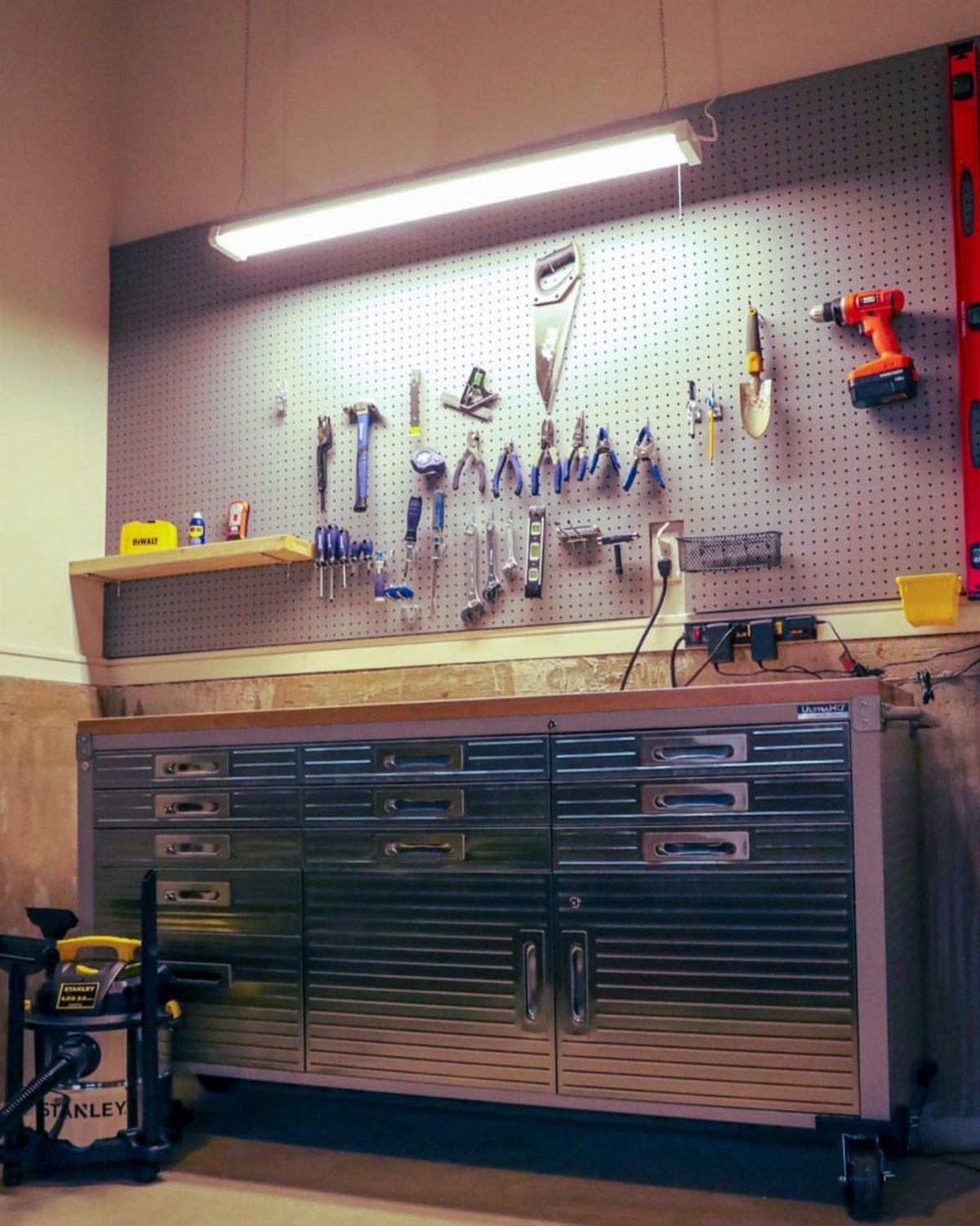 Garage Workbench Ideas: 11 Builds from IKEA Hacks to Heavy-Duty 6 A large silver metal rolling tool cabinet positioned under a tool-filled pegboard wall.