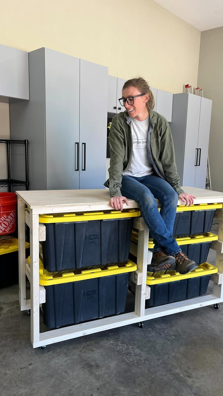 Garage Workbench Ideas: 11 Builds from IKEA Hacks to Heavy-Duty 10 A woman sitting on a white wooden workbench with large black and yellow storage bins underneath.