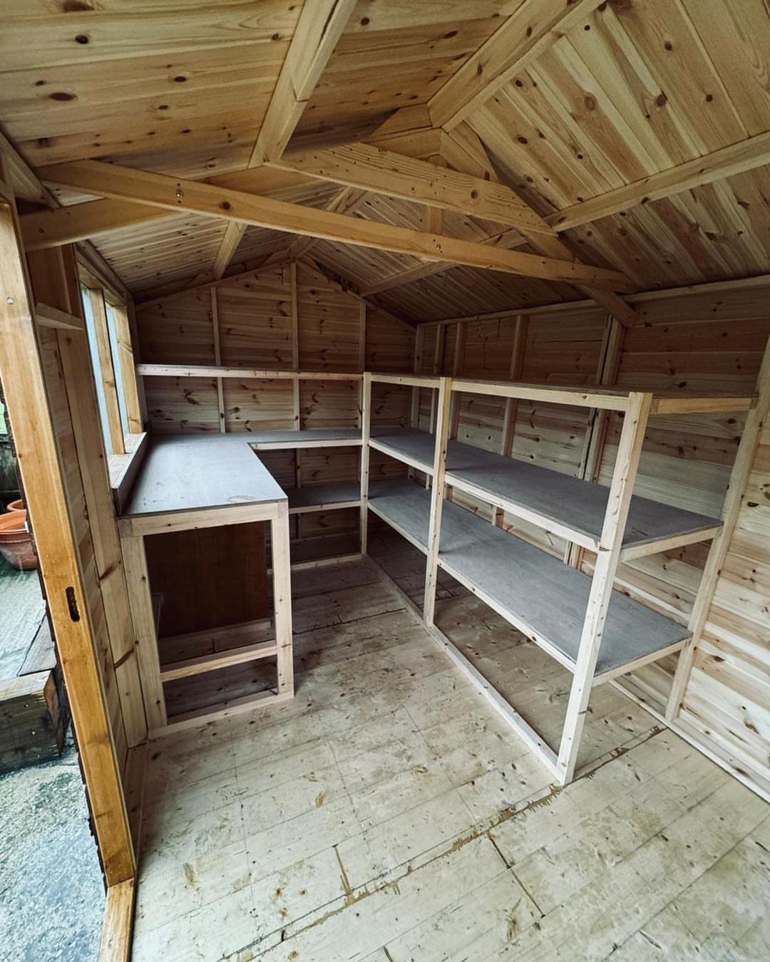 Built-in wooden shelving units and a workbench inside an empty wooden garden shed.