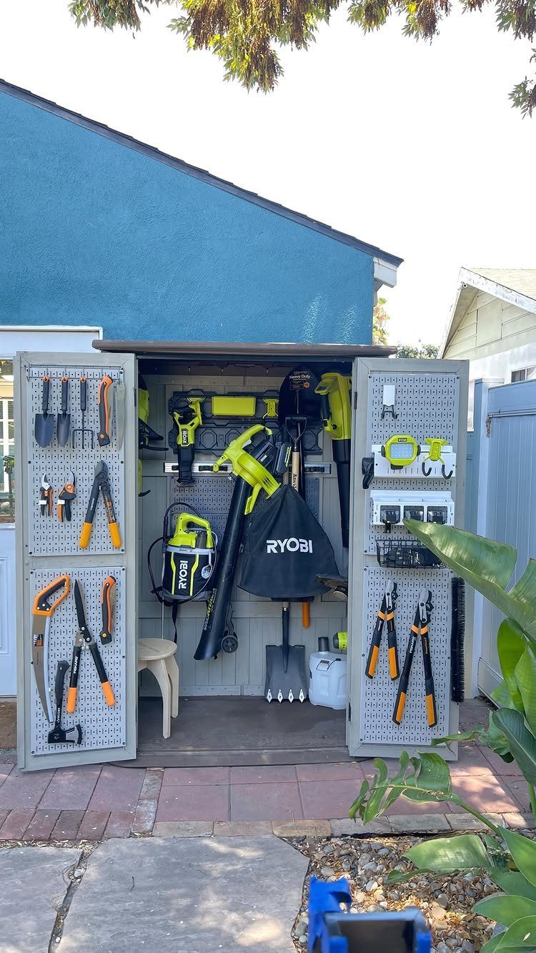 Garden tools hanging on pegboards inside an open, organized blue garden shed.