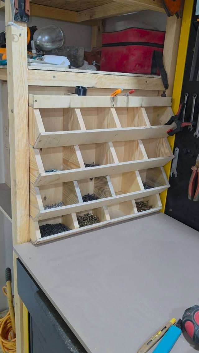 Wooden organizer with multiple compartments filled with small metal screws mounted on a workshop workbench.