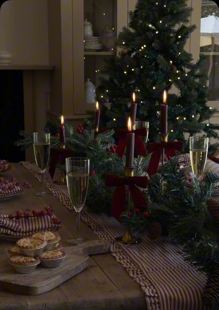 Festive table setting with evergreen garland, lit candles, champagne flutes, and pastries on wood.