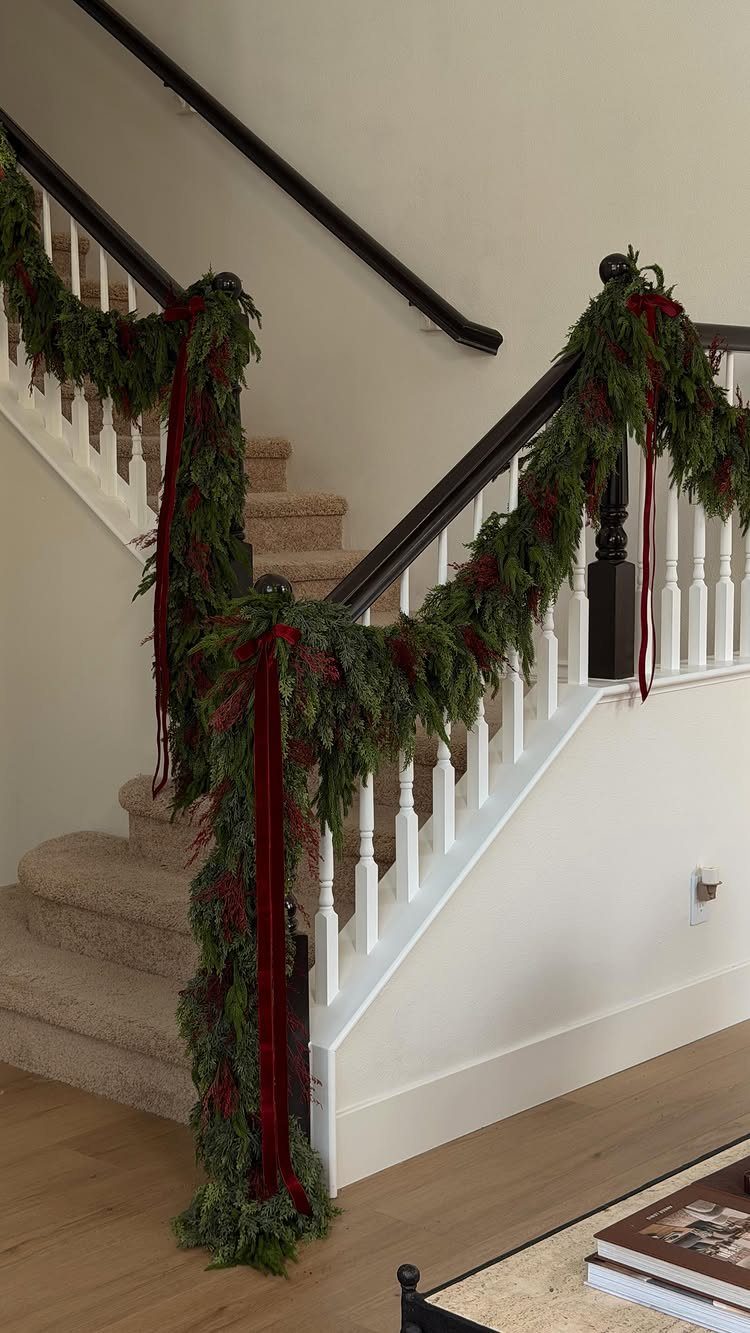 Green evergreen garland with red velvet ribbons draped along a white staircase banister.