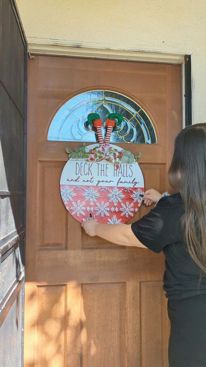A person hanging a circular holiday sign on a wooden front door.