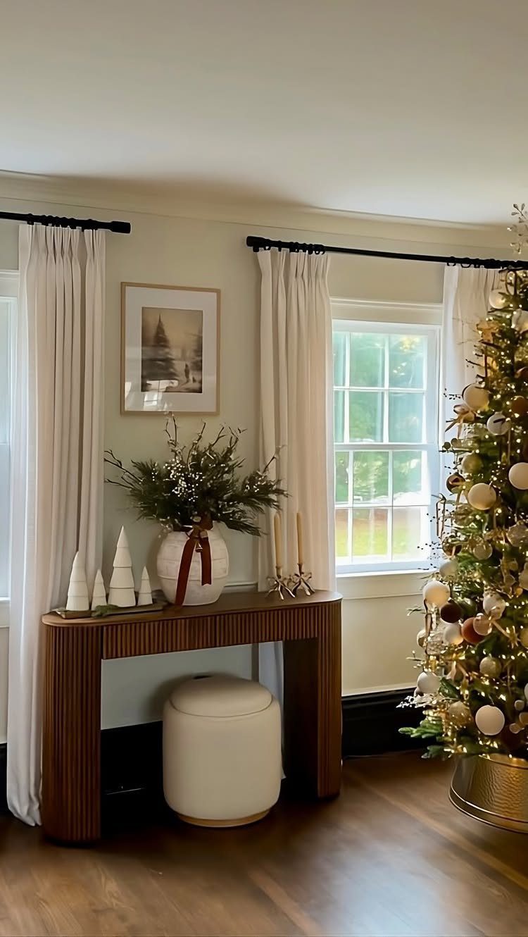 A wooden console table decorated with evergreen branches, white ceramic trees, and candles in a living room.
