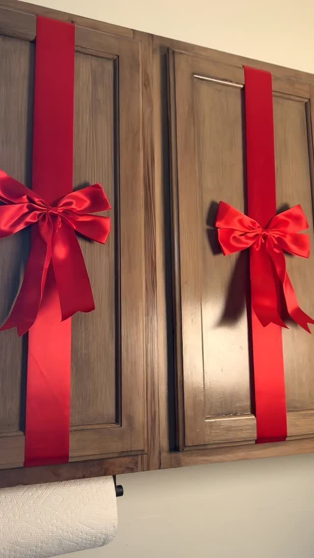 Red satin ribbons with large bows tied vertically on wooden kitchen cabinet doors.
