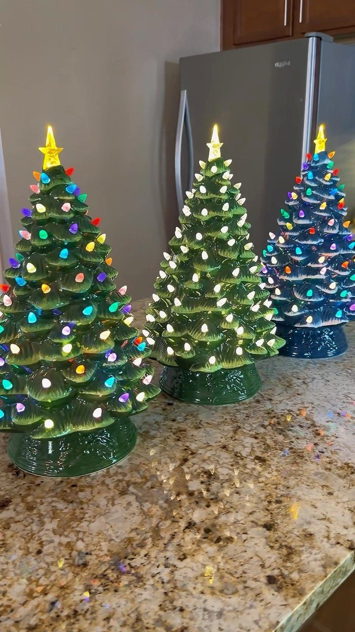 Three small glowing ceramic Christmas trees sitting on a granite kitchen countertop.