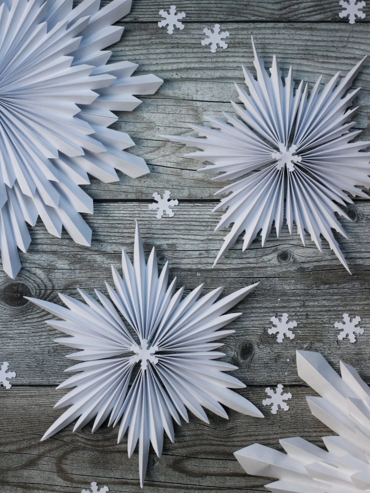Homemade Christmas Ornament Ideas: 8 Easy Projects 7 White pleated paper starburst ornaments scattered on a weathered grey wooden plank background.