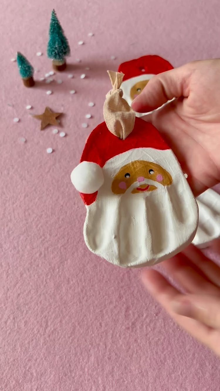 Hand holding a handmade Santa Claus ornament made from white cornstarch dough on pink background.