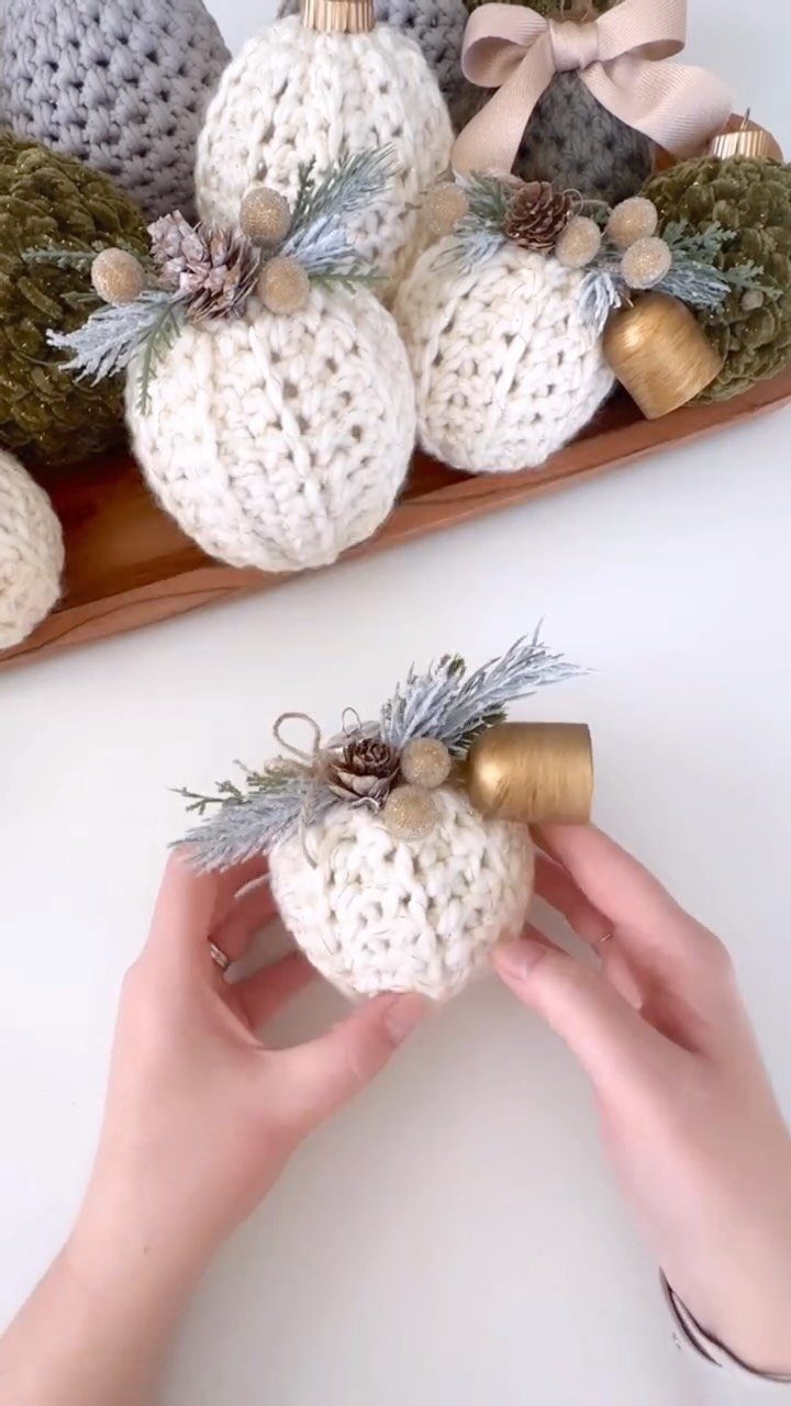 Hands holding a white crocheted Christmas ornament decorated with pinecones and a gold bell.