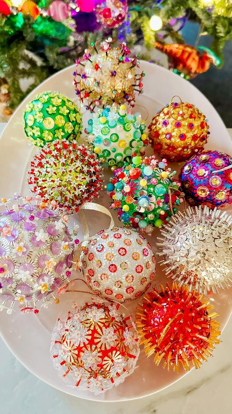 Various colorful handmade Christmas ornaments decorated with beads and sequins on a white plate.
