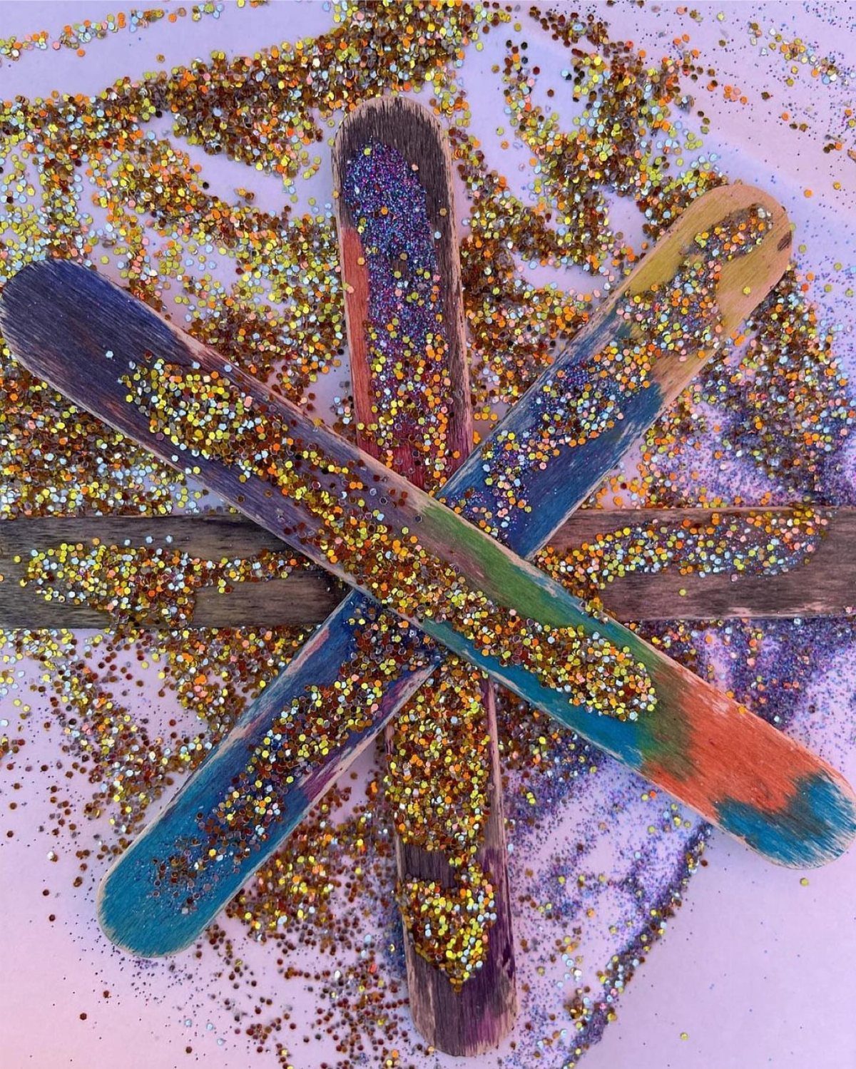 Glitter-covered wooden popsicle sticks arranged in a star pattern on a glittery surface.