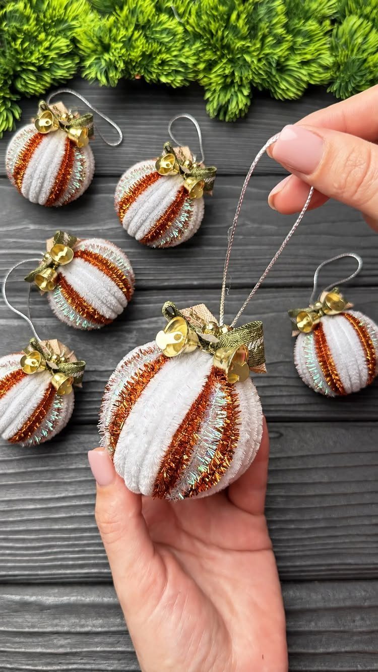 Hand holding a white and orange glittery striped Christmas ornament against a dark wood background.
