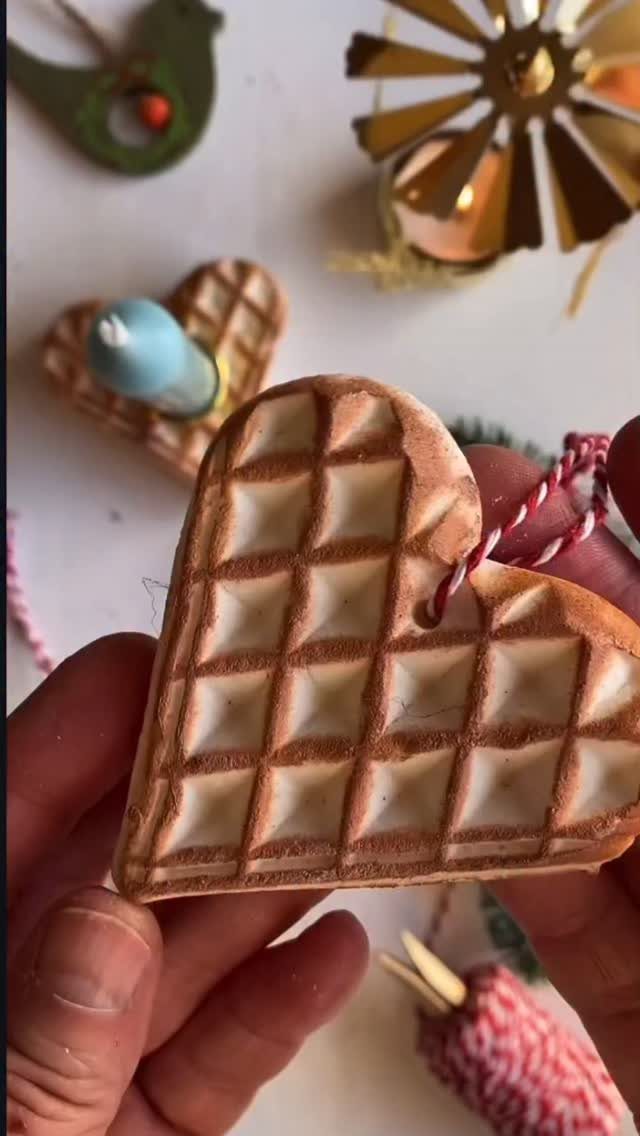 Hands holding a heart-shaped waffle ornament with a red and white hanging string.