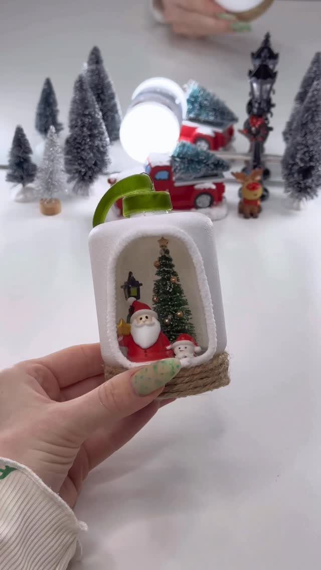 A hand holding a small white dome ornament featuring a miniature Santa and Christmas tree scene.