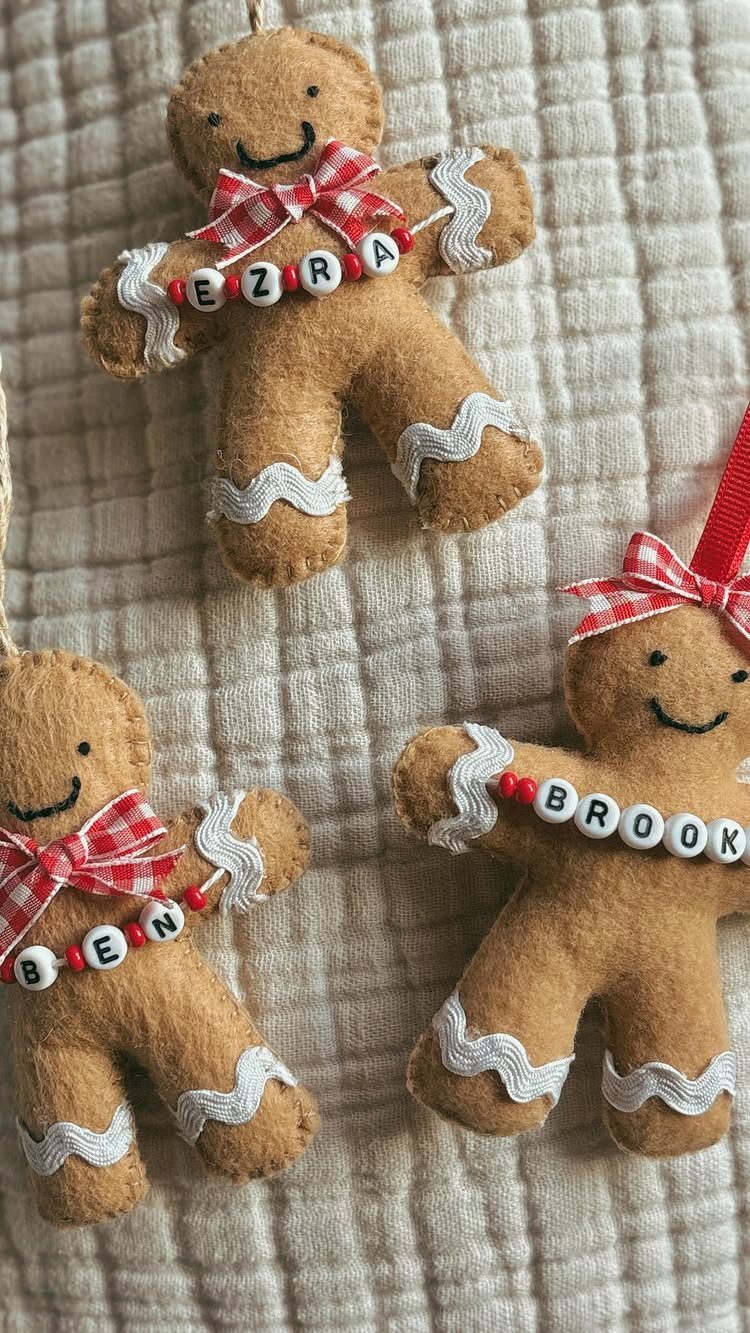 Three felt gingerbread man ornaments with name beads and red checkered bows hanging on white fabric.