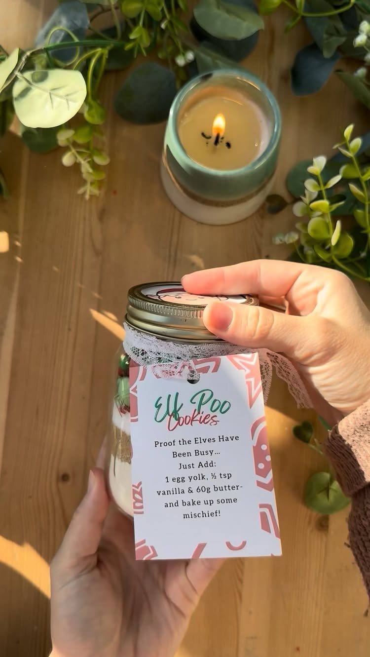 Hands holding a mason jar filled with layered cookie ingredients and a decorative tag.