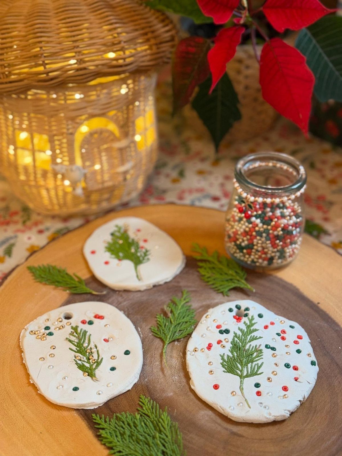 Three white clay ornaments decorated with green sprigs and colorful beads on a wooden plate.