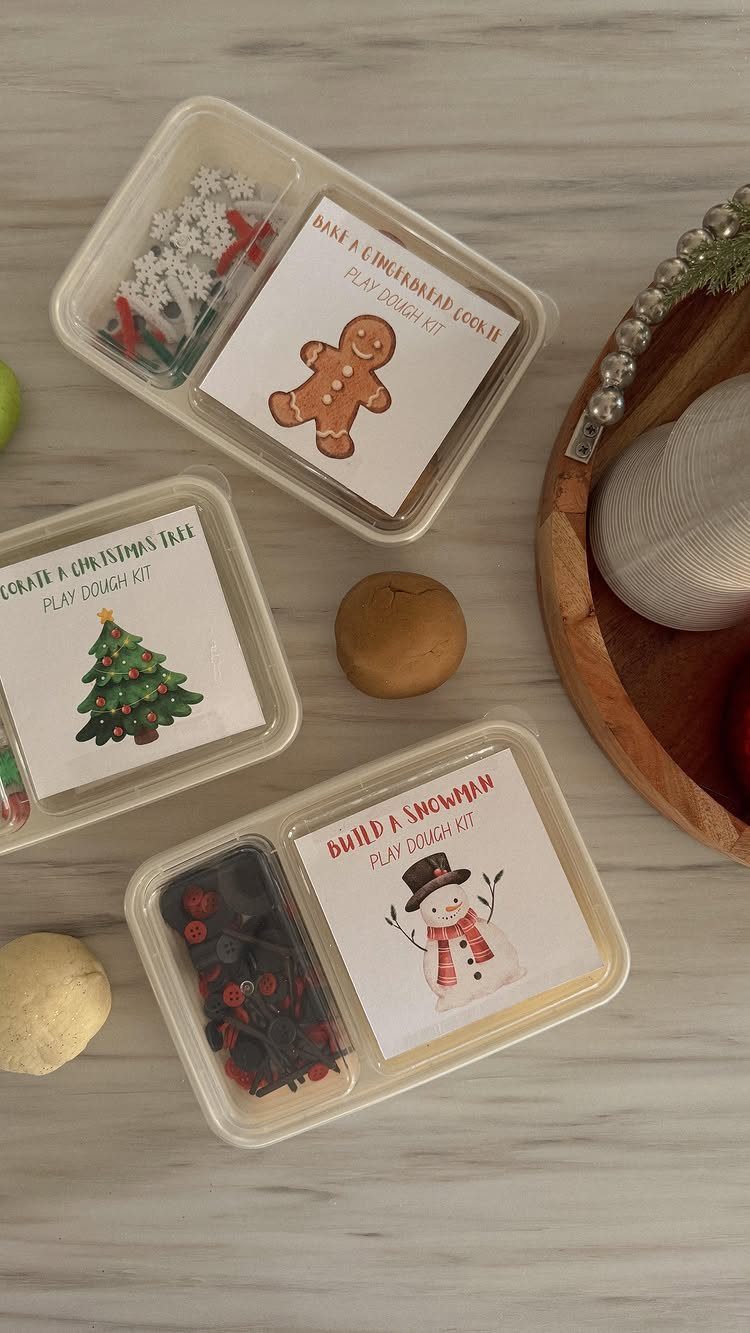 Three clear plastic containers containing colorful playdough and festive decorations with printed labels.