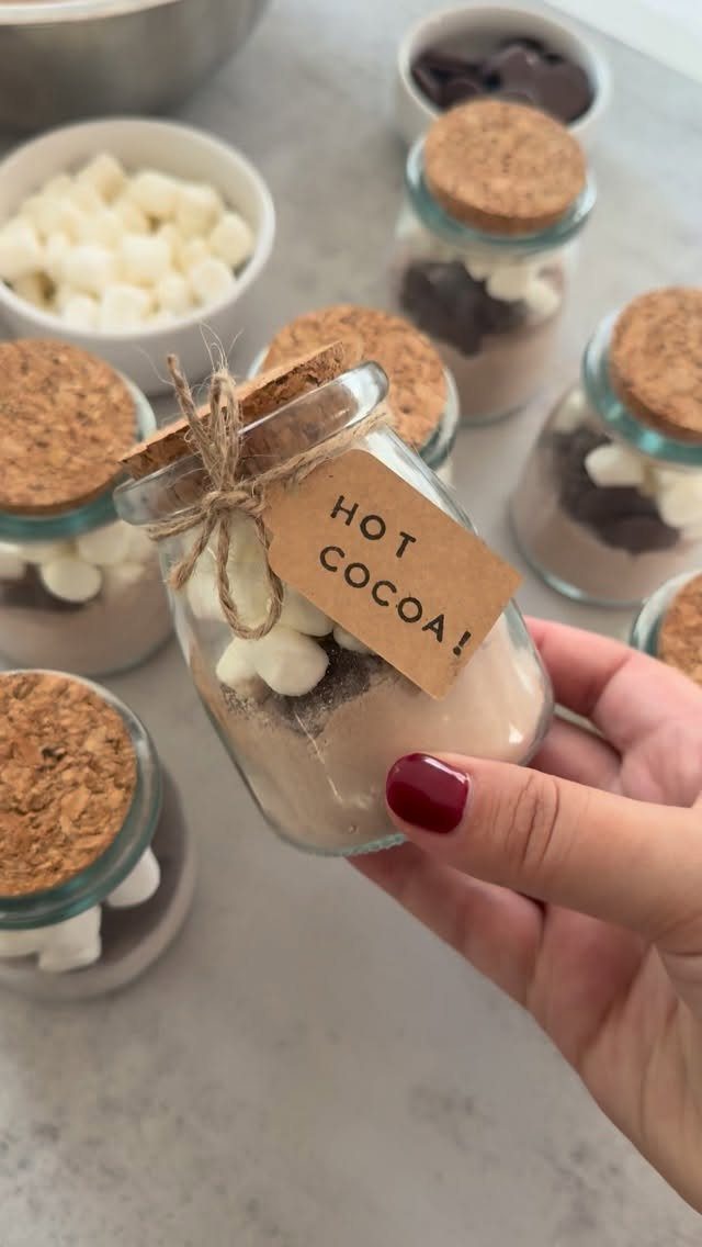 A hand holding a glass jar filled with layered hot cocoa mix and mini marshmallows.