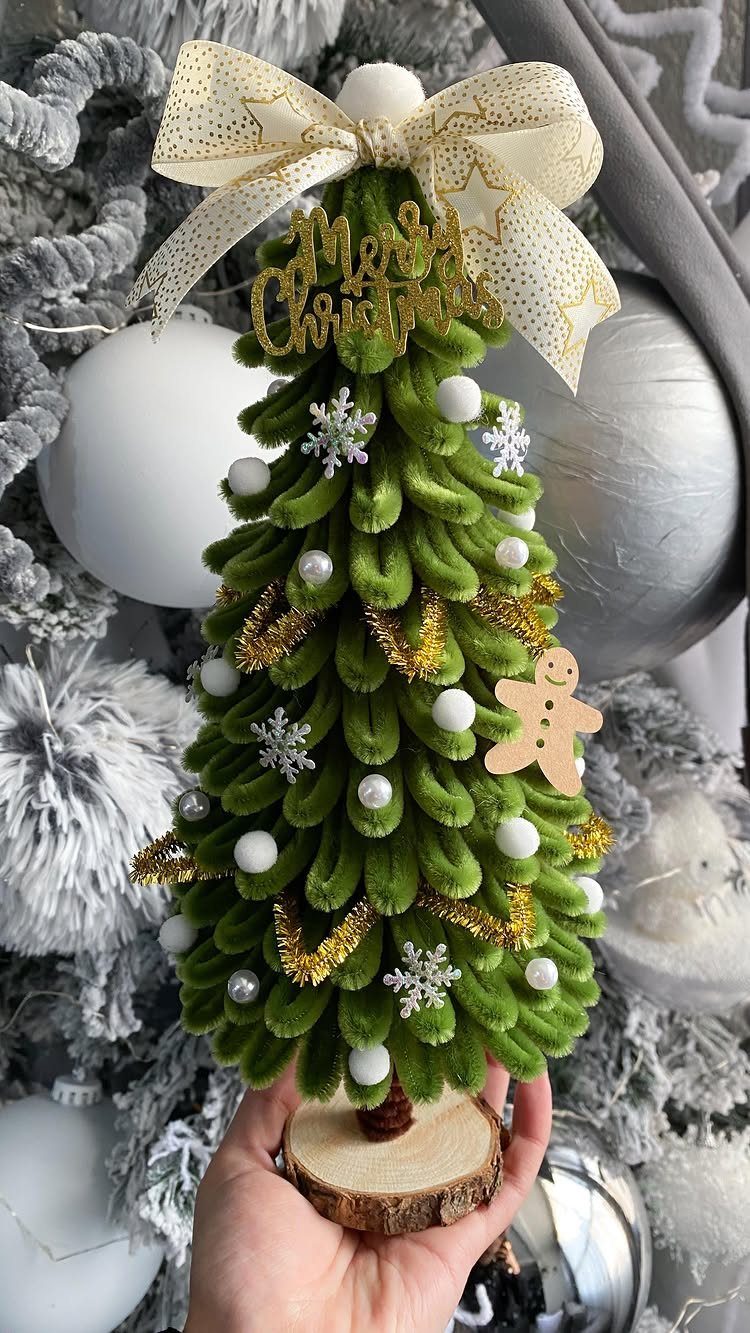 A small green pipe cleaner Christmas tree decorated with pearls and gold glitter held in a hand.