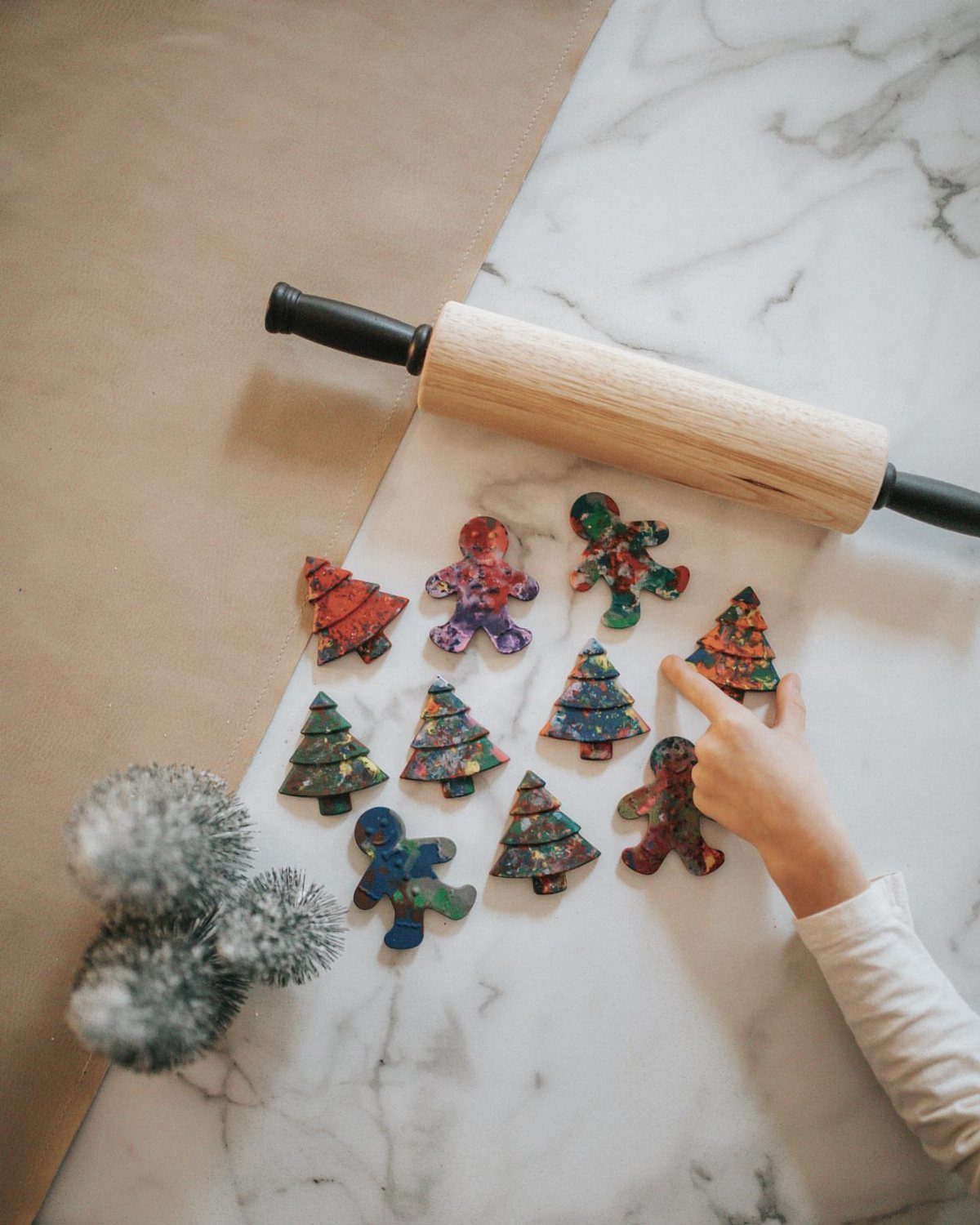 Colorful shaped crayons in gingerbread man and Christmas tree designs on a marble tabletop.